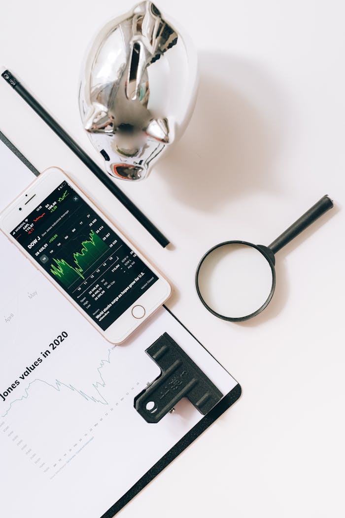 Flat lay of financial tools including smartphone, magnifying glass, and stock data for business insights.